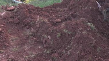 Endüstriyel kazıcı taşlarla kil toprağı topluyor. Kazı süreci tam gaz devam ediyor, kova toprağı kaldırıyor ve taşıyor, kazı, yol çalışması ve vakıf hazırlığı için gerekli.