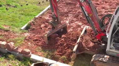 Kazı makinelerinin kovası toprağı kazarken toprak ve taşlarla dolu. Güçlü makine inşaat alanında çalışıyor, projenin bir sonraki aşaması için zemin hazırlıyor..
