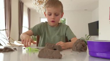 Odaklanmış bir çocuk kinetik kumla oynar, masaya bastırır ve şekillendirir. Güzel motor becerileri ve yaratıcı düşünceleri destekleyen yaratıcı ve dokunaklı bir oyun aktivitesi..