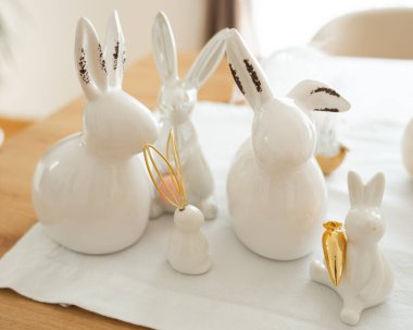 Porselen tavşan heykelcikleri, bazıları altın aksanla süslenmiş, beyaz bez bir yüzey üzerine dizilmiş. Şirin ayar neşeli ve zarif Paskalya dekorunu vurguluyor. 