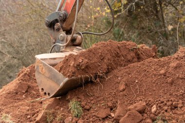 Toprağı eşeleyen toprak ve taşlarla dolu bir kazı kovası. Ağır makineler bir inşaat sahasında çalışıyor ve daha fazla iş için zemin hazırlıyor.