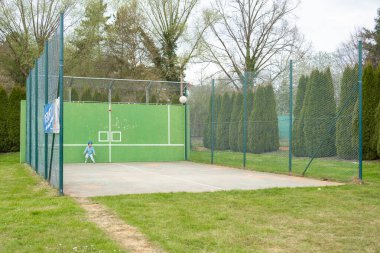 Spor kıyafetli çocuk yeşil duvarlı bir sahada topla oynuyor. Doğal ortam, tek başına hareket etmek ve çocukluk gelişimi, spor güvenliği ya da aktif yaşam tarzı kampanyaları için mükemmel bir yer..