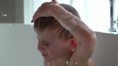 Gözleri kapalı genç bir çocuk, küvetteki bir su akıntısı altında kendini sakin hissediyor. Etrafındaki su damlacıkları, neşeli bir huzur hissi yaratıyor.. 