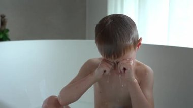 Gülümseyen çocuk, kafalarına su dökmek için mavi bir oyuncak kova kullanarak eğlenceli bir banyo yapmayı seviyor. Neşeli an, neşeli bir banyo ortamında tasasız bir çocukluk yakalar..