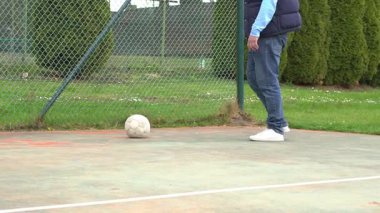 Adamın biri parkta beyaz bir futbol topunu tekmeliyor. Yakın plan dinamik hareketi, spor ayakkabıları ve topun canlı yeşil bahar ağaçlarına karşı olduğunu gösteriyor..
