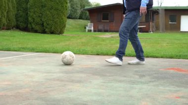Kot pantolonlu atletik bir adam futbol topunu tekmeliyor. Yeşil park arka planına sahip yakın plan çekimleri enerji, spor ve açık hava aktivitelerini yansıtıyor..
