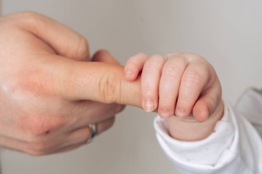 Yetişkin parmağını nazikçe tutarak güven, ilgi ve ebeveyn sevgisini sembolize eden küçük bir bebeğin yakın çekimi. Ebeveyn ve çocuk arasındaki bağı yakalayan hassas bir an. Yüksek kalite fotoğraf