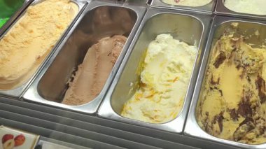 Çikolata, vanilya ve daha fazlasının yer aldığı metal kaplarda çeşitli dondurma çeşitleri ve cazip bir ikram için renkli kremalı dokular..