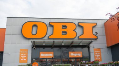 Bad Hersfeld, Almanya, 04.20.25. OBI mağazasının ön tarafında Ausgang ve Eingang etiketli cesur tabela ve giriş var. Dış kısımda çalışma saatleri vurgulanıyor ve dekoratif bitkiler sergileniyor.