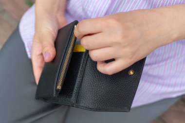 Finansal bir işlem ya da satın alma olduğunu gösteren bir kartı çıkarmak için siyah bir cüzdan açan ellerin yakın çekimi. Odak noktası cüzdan ve el hareketi..
