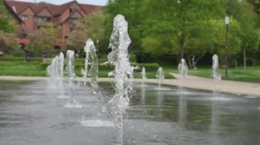 Güneşli bir günde parklardaki etkileşimli fıskiyelerde su püskürtmek. Su sıçraması yeşil ağaçlar ve patikalar arasında dinamik ve ferahlatıcı bir manzara yaratır..