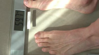 Kişi kilogram ağırlığını gösteren dijital bir ölçekte duruyor. Görüntü, vücut ağırlığının sağlık veya yaşam tarzı yönetiminin bir parçası olarak kendini izlemesini yakalar..