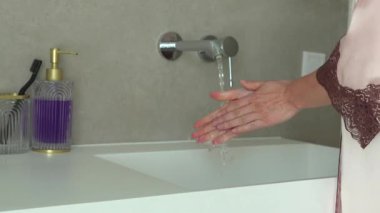 Modern bir banyoda, musluğun altında sabun ve aksesuarlarla yıkanan eller. Rahat bir ortamda temizlik ve hijyene vurgu yapar.