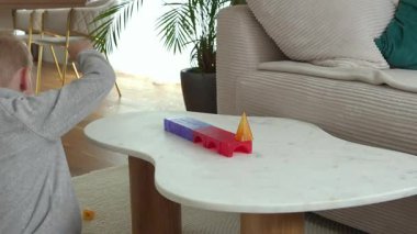 Genç bir çocuk, beyaz bir masada canlı yapı taşlarıyla yaratıcı bir oyun oynuyor, erken gelişim becerilerini ve rahat bir oturma odasında el-göz koordinasyonunu gösteriyor..