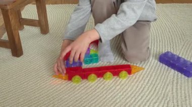Çocuk halı döşeli bir zeminde manyetik bloklar kullanarak renkli bir oyuncak tren inşa ederek yaratıcı bir oyuna girişiyor. Hayal gücü ile öğrenme ve geliştirme.