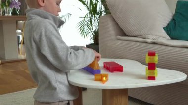 Küçük bir çocuk, rahat bir oturma odasında, yuvarlak bir masada renkli manyetik bloklarla yaratıcı oyunlar oynuyor. Odaklanmış ve yaratıcı oyuncu aktivite geliştirme.