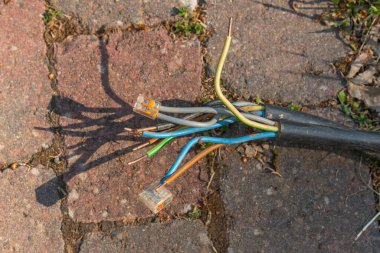 Kırsal tuğla kaldırımda yıpranmış elektrik kabloları var. Görünür renkli kablolar, potansiyel güvenlik tehlikesini vurguluyor. Kablo onarımına veya yedeğe ihtiyaç duyulduğunu vurgular.