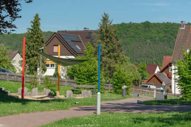 Renkli direkleri ve güneş kremi olan huzurlu bir banliyö parkı manzarası. Güneş panelleri ve yemyeşil yaprakları olan konutlarla çevrili..