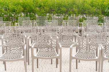 Açık havada dizilmiş boş sandalyeler simetrik bir bahçe sahnesi oluşturuyor. Sandalyelerin karmaşık tasarımı açık havaya sanatsal bir dokunuş katıyor..