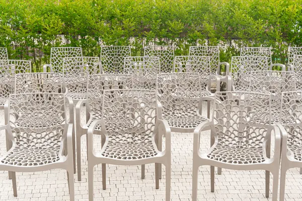 Açık havada dizilmiş boş sandalyeler simetrik bir bahçe sahnesi oluşturuyor. Sandalyelerin karmaşık tasarımı açık havaya sanatsal bir dokunuş katıyor..