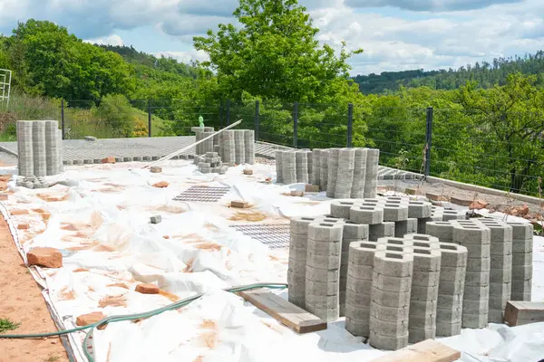 Doğal yeşilliklerle çevrili bir inşaat sahasına beton bloklar yığılmış. Beyaz branda zemini kaplayarak, bölgeyi bina faaliyetlerine hazırlıyor.