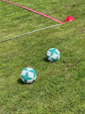 Futbol topları çimenli bir sahada antrenman için hazırlanmış koni setinin yanına yerleştirildi. Kırmızı koni ve beyaz çizgi işaretleyicisi spor antrenmanlarını geliştiren bir eğitim bölgesini gösteriyor..