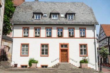 Tahta bir çatı ve çiçek kutularıyla dolu birden fazla penceresi olan tarihi Alman binası. Giriş, ahşap kapıya çıkan adımlarla vurgulanır. Geleneksel mimariyi yakalar. Kötü karakterleri.