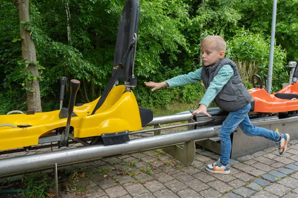 Genç bir çocuk yemyeşil bir parkta raylarda sarı bir pedal arabasını itiyor. Çocuk heyecanlı ve odaklanmış, açık hava oyunlarının ve maceraların neşesini yakalıyor..