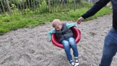 Yuvarlak bir oyun parkında neşeli bir şekilde dönen bir çocuk, gündelik giysiler giyer ve tasasız görünür. Sahne, açık hava parkında neşeli bir heyecan anı yakalıyor..