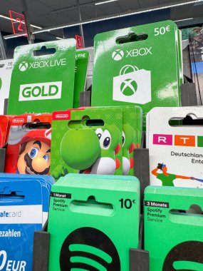 Bad Hersfeld, Almanya, 12.06.25. Xbox, Nintendo ve Spotify gibi çeşitli hediye kartlarının bir mağazada sergilenmesi, oyun ve müzik tutkunları için popüler seçenekler sunuyor. Kartlar dikey olarak sıralanmış
