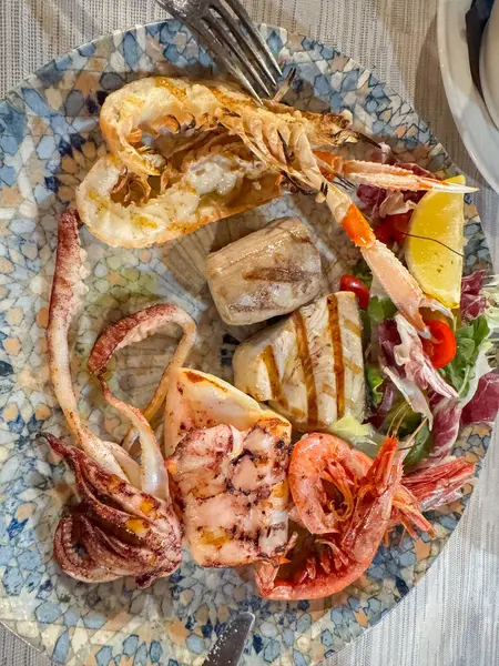 İçinde karides, mürekkep balığı ve taze salata ve limon dilimleri bulunan ızgara deniz ürünleri tabağı. Deniz ürünleri temalı yemek ya da mutfak sunumu için mükemmel..