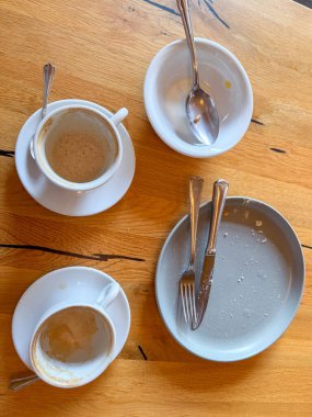 Ahşap bir masanın üzerinde duran kahve fincanları ve tabaklar yakın zamanda bitirilmiş bir yemek ya da mola olduğunu gösteriyor. Görüntü yemek sonrası ya da kahve sonrası görüntüler..