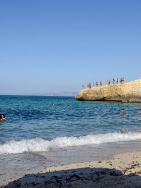 İnsanlar plajda yüzmenin ve güneşli bir günde bir uçurumdan açık mavi sulara atlamanın heyecanını tatmak için toplandılar. Sahne yaz eğlencesinin özünü yakalar deniz kıyısında.