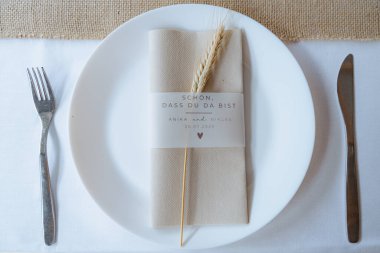 Beyaz tabak, çatal bıçak takımı ve içinde buğday ve kişisel metin bulunan dekoratif peçeteyle kırsal bir düğün yerinin yakın çekimi. Olay tasarım kavramları için mükemmel