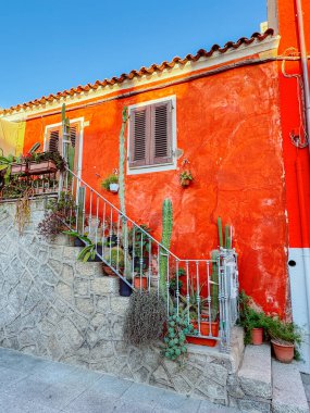 Sardinya 'da taştan merdivenleri, kaktüsleri ve Akdeniz bitkileriyle süslü kırmızı bir ev. Seyahat, mimarlık, yaşam tarzı, ev dekorasyonu, turizm ve emlak projeleri için mükemmel bir sahne.