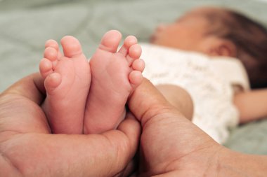 Küçük yeni doğmuş ayaklar, sevgi, ilgi ve aile bağını simgeleyen bir ebeveynin ellerinde şefkatle kucaklanır. Bu samimi an ebeveynliğin özünü ve yeni hayatın mucizesini yakalar.