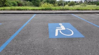 Erişilebilir park yeri, asfaltta mavi tekerlekli sandalye sembolü ile işaretlenmiş. Bu da engelliler için ayrılmış park yerini gösteriyor. Doğal bir ortamla çevrili, kamusal alanlarda kapsayıcılığı teşvik ediyor.