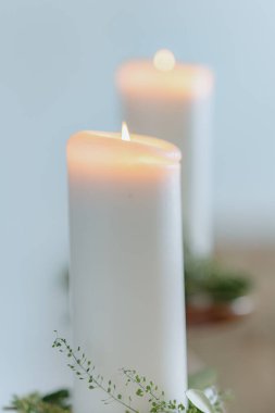 Beyaz mumlar, narin yeşilliklerle çevrili yumuşak bir şekilde parıldıyor. Huzurlu ve rahatlatıcı atmosfer sıcaklığa ve sükunete odaklanmayı artırır. Huzurlu ortamlar ve meditasyon anları için mükemmeldir.