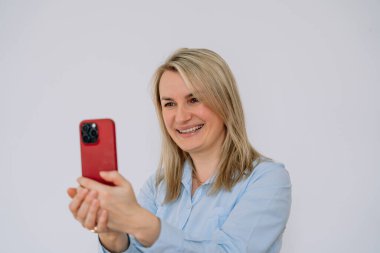 35-37 yaşlarında, Avrupa görünümlü, mavi tişörtlü, cep telefonuyla video görüşmesi yapan bir kız. Yüksek kalite fotoğraf