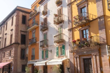 Bosa, güneşli bir günde renkli cepheli ve dekoratif balkonlu çok katlı binalar. Mimari detaylar ve çiçek saksıları sahneye cazibe ve karakter katar..