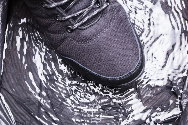 Black mens sneakers with drops of water, close-up on a black isolated background.