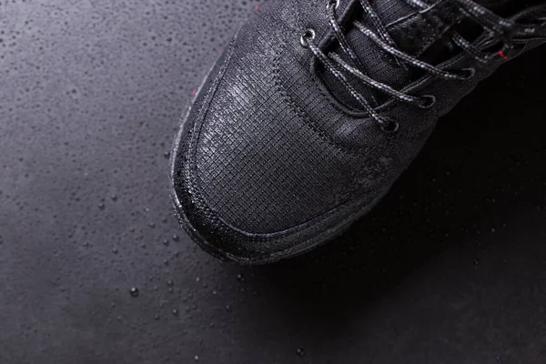 Black mens sneakers with drops of water, close-up on a black isolated background.