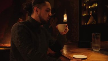 Koyu bir barda bir adam beyaz bir bardaktan kahve içer..