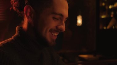 Portrait of a happy smiling man in a sweater indoors in dark light. The guy looks at the smartphone.