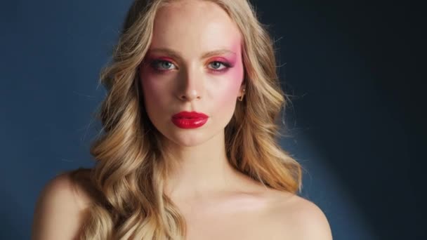 明るいメイクと赤い唇で美しいモデル 青い背景の少女のクローズアップの肖像画 — ストック動画
