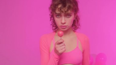 Pembe bir arka planda, lolipop yiyen alımlı, güzel bir kadın manken. Kız şeker yalıyor.