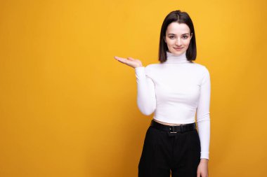 Reklam konsepti. Genç bir kız, sarı bir arka plan hakkında bilgi almak için elini fotokopi alanının kenarına doğrultuyor..