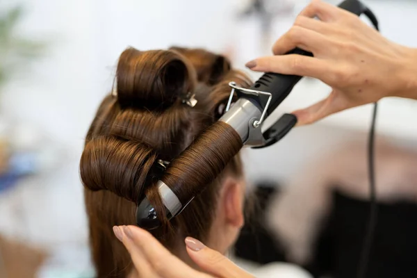 The hairdresser curls the models hair. Curling iron for curling hair close-up.