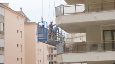 Tarragona, İspanya - Haziran 02 2023: İnşaatçılar evin yüksekliğinde bir ön cephe asansöründe bir yumrukla çalışıyorlar.