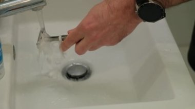 Cleaning shaving razor in bathroom sink. Rinsing off razor with water.